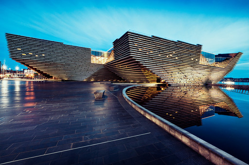 Nighttime view of the V&A Dundee, with reflections of the building in the adjacent pool.