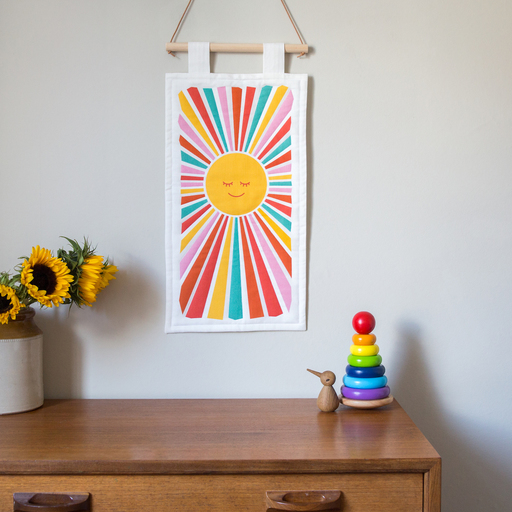 A wall hanging of the sun, with multi coloured rays emitting from its centre. 