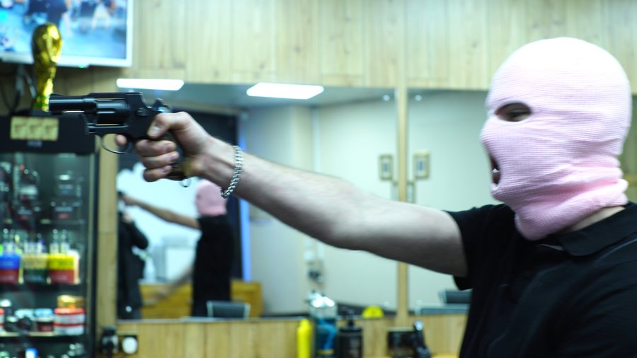 A figure wearing a pink balaclava and black T-shirt points a gun out of shot; a still from the music video for Diamonds Into Dust