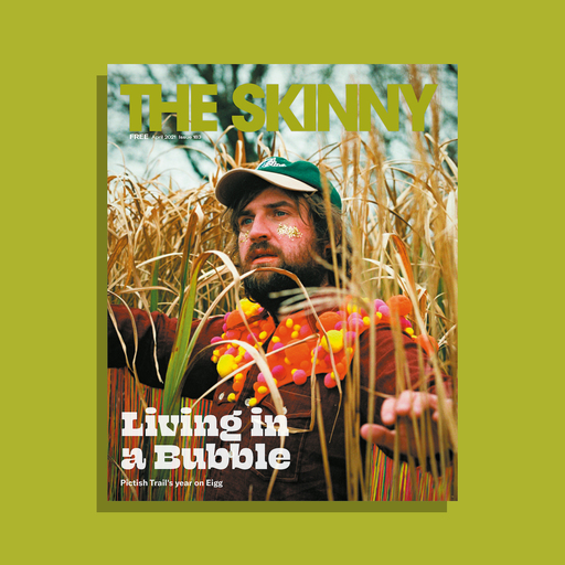 The cover of The Skinny's April 2021 issue; Johnny Lynch stands in the centre of the frame, surrounded by tall grass. Headline reads 'Living in a Bubble'