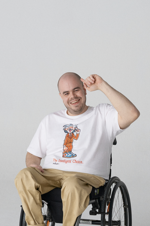 A portrait photograph of Wheelman - he wears khaki trousers and a white t-shirt with an illustration of Albert Einstein and the caption 'The Intelligent Choice'.