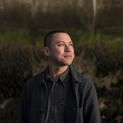 Portrait photo of Paul Sng. Paul stands in the foreground looking off to the right of shot, with trees and grass in the background