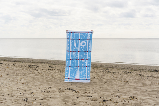 A beach towel on a sandy beach - the towel depicts swimming scenes in blue and white with flashes of red.