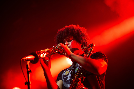 Kaidi Akinnibi of black midi playing a clarinet amid a flash of red and orange light on stage at Edinburgh International Festival. He has a saxophone strapped around his shoulder.