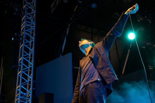 Damon Albarn on stage at Edinburgh International Festival. He stands with one hand outstretched holding a microphone; he wears a dark jacket, shirt and jeans.