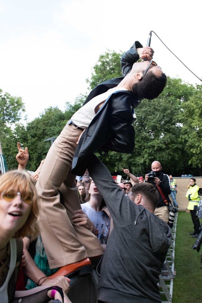 The Murder Capital frontman James McGovern stands on the crowd barrier at TRNSMT festival. His head is turned towards the sky, and he holds a microphone to his mouth. He is being held up by a security guard, while a crowd forms in front of him.
