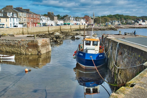 A blue and white fishing boat in a small harbour, with a row of small buildings behind it.