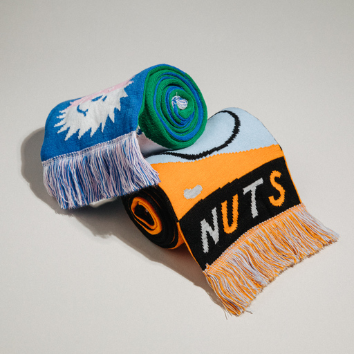 A pair of rolled-up scarves. Top scarf is green and blue, with a sun-like figure visible; bottom scarf is orange, blue and black, with the word 'NUTS' visible.