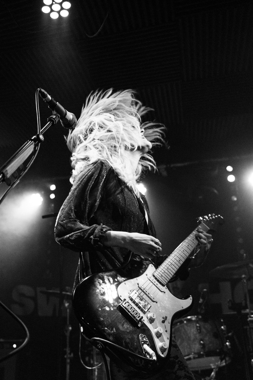 Black and white photo of Alice Johnson playing a guitar on stage, with a microphone stand in front of her.