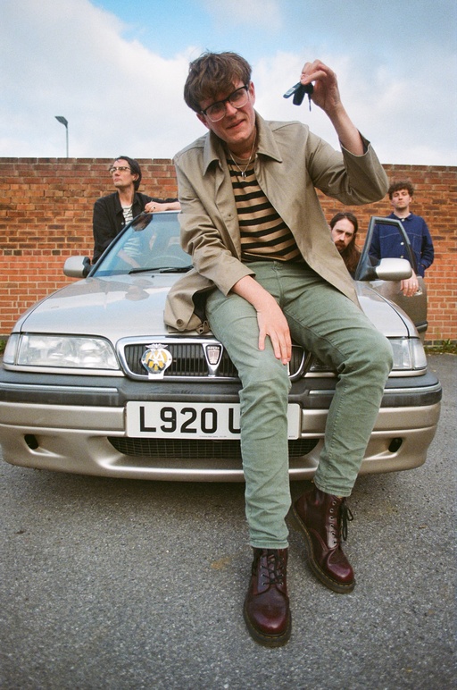 Yard Act pictured next to a Rover car; lead singer James Smith stands at the front of the group, dangling car keys.
