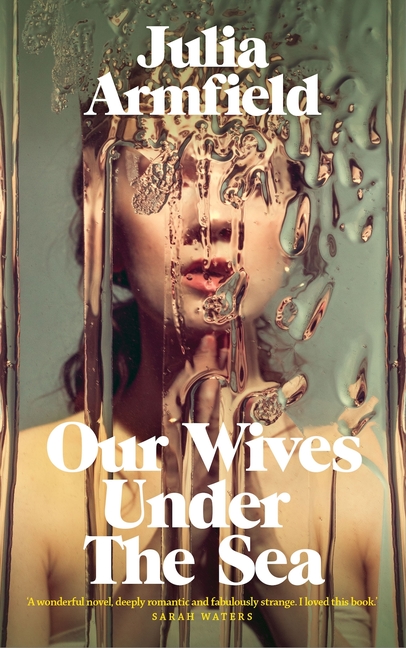 The cover of Our Wives Under the Sea by Julia Armfield. A woman stands behind a warped pane of glass.