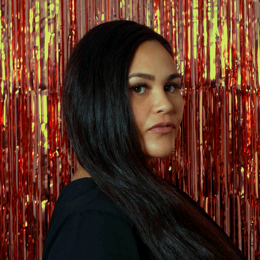Amanduh Wilkinson, standing side-on in front of a wall of red and gold tinsel.