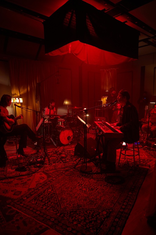 Fontaines D.C. performing; the band sit in a circle by their instruments, beneath a large red light.