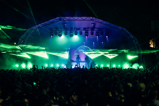 An electronic artist plays for a large crowd under blue and green lights