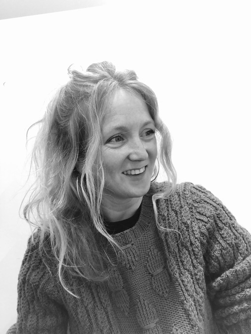 Photo of Hollie McNish, wearing a woolen sweater and smiling.
