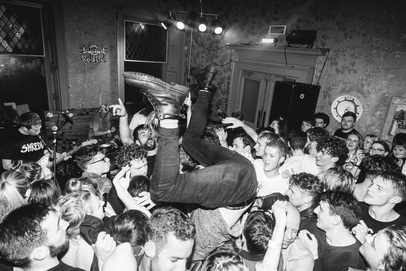 A black and white image of a crowd at the Tenement Trail festival, where one person is being held upside down