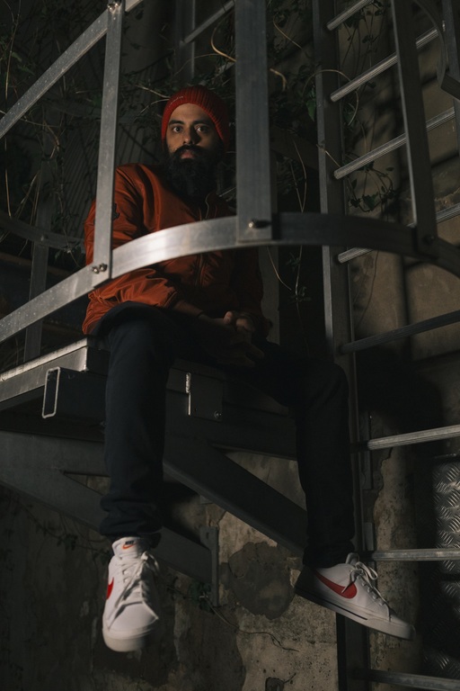 Kapil Seshasayee sits inside a metal fire escape. He wears a red hat and red jacket.