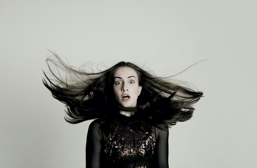 Portrait photo of Julia Masli. She wears a sparkly brown top, and her hair is flying upwards.