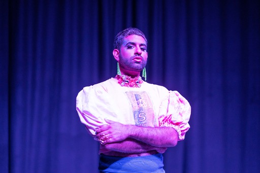 Alok Vaid-Menon stands on stage under a purple light.