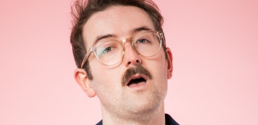 Sam Lake looks into the camera, with his mouth slightly open, in front of a pink background.