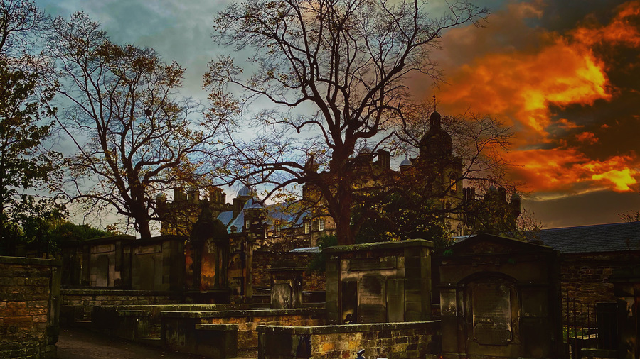 Greyfriars Kirkyard at sunset. The trees are bare and a red sunset is forming over the buildings.