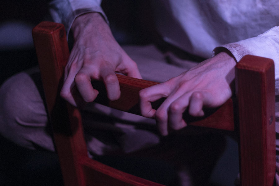 A pair of white hands gripping on to the back of a wooden chair.