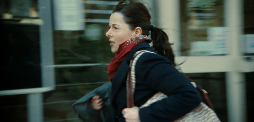 A still from Full Time; a woman carrying a coat in one hand and bag in the other walks briskly down a street