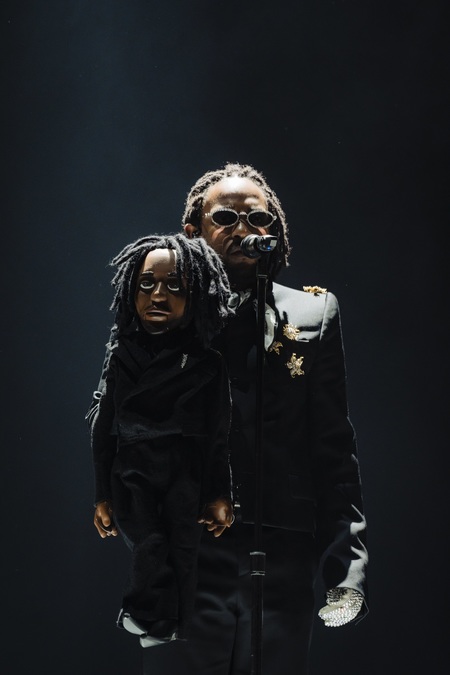 Kendrick Lamar dressed all in black, holding a small puppet version of himself.