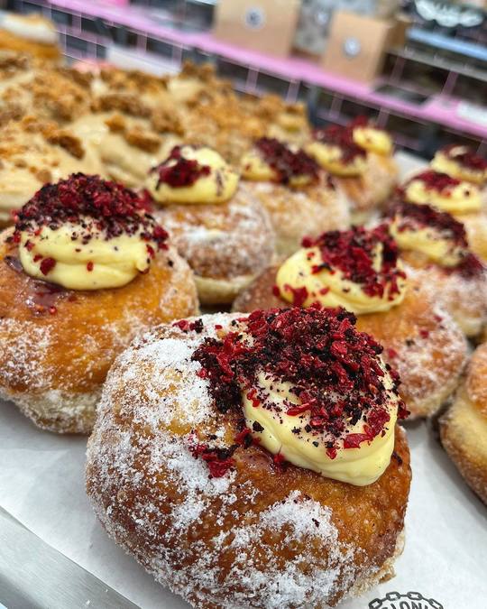 A tray of doughnuts topped with custard and red flakes.