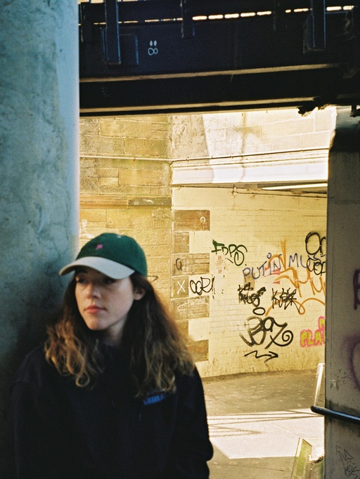 Berta Kennedy, standing in front of a wall with graffiti tags on it