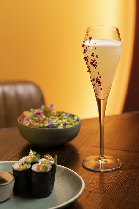 A flute-shaped glass with red flakes on the outside; two small dishes of food are also visible.