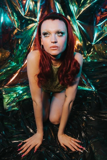 A model crawling towards the camera, in front of a shiny metallic green backdrop.
