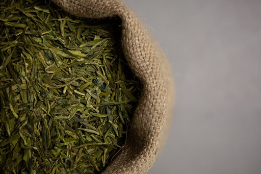 A cloth sack filled with strands of green tea.