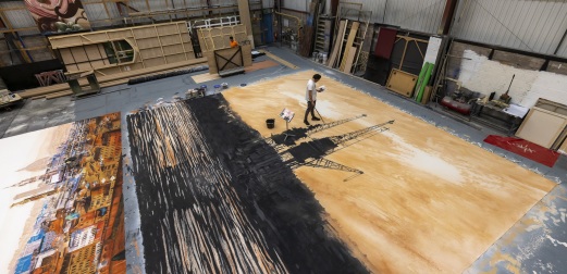 An artist works on a large-scale backdrop of Glasgow at Scottish Opera's rehearsal space