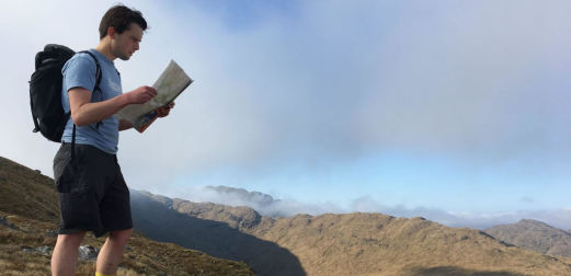 Kieran Hodgson reads a map standing on a remote hill.