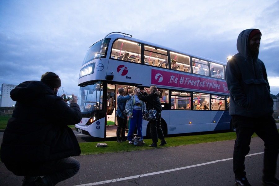 A make-up artist applies make-up to an actor standing in front of a bus.