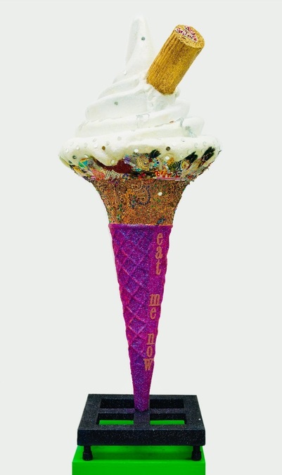 An oversized ice cream cone with a glittery edge; the words 'eat me now' are written vertically down the cone.