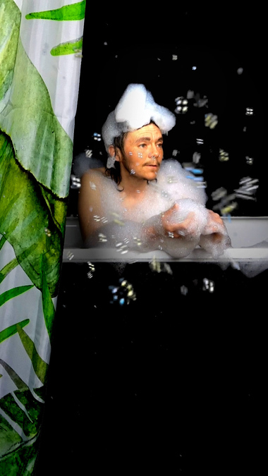 A figure sits up in the bath, covered in bubbles.