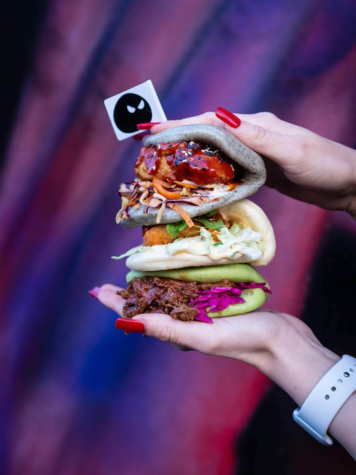 Three bao buns with various fillings, held up against a purple and blue background.