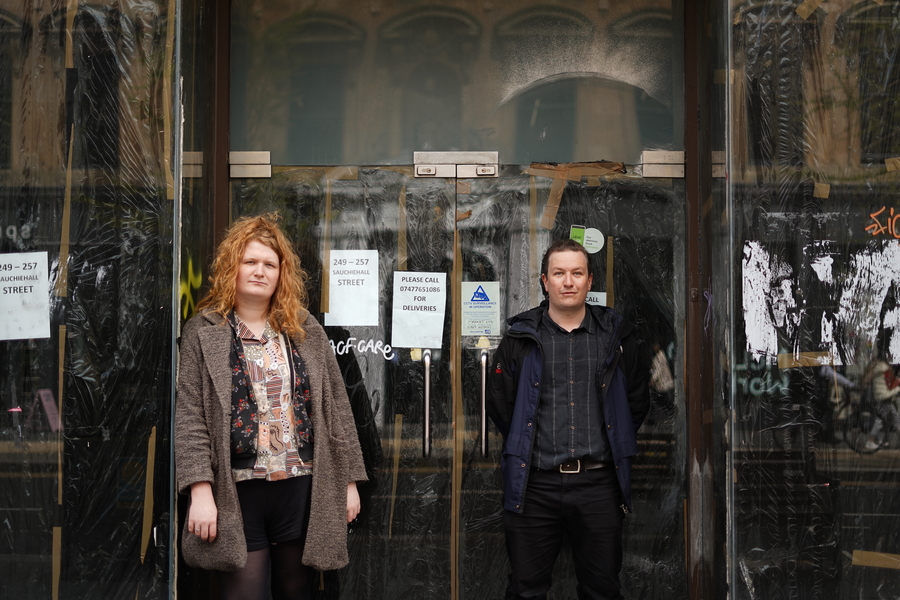 The two members of comfort, standing in front of a doorway marked with graffiti.