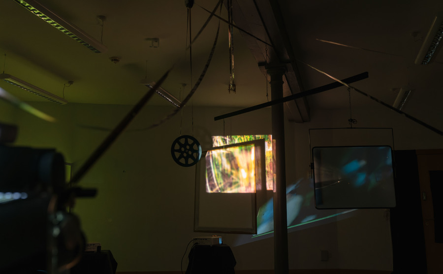 A room with a number of screens dotted around; a film is being projected onto the back wall.
