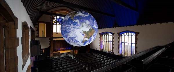A sculpture of the earth hanging above church pews.