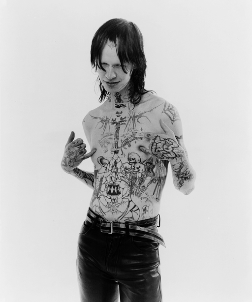 Photograph of a shirtless tattooed figure against a white background.