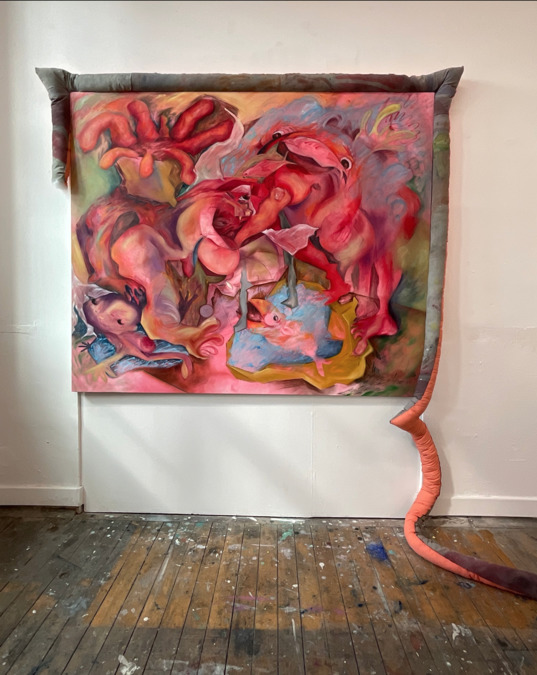 A large artwork hung on a studio wall. The piece has a tail-like appendage which runs to the floor.