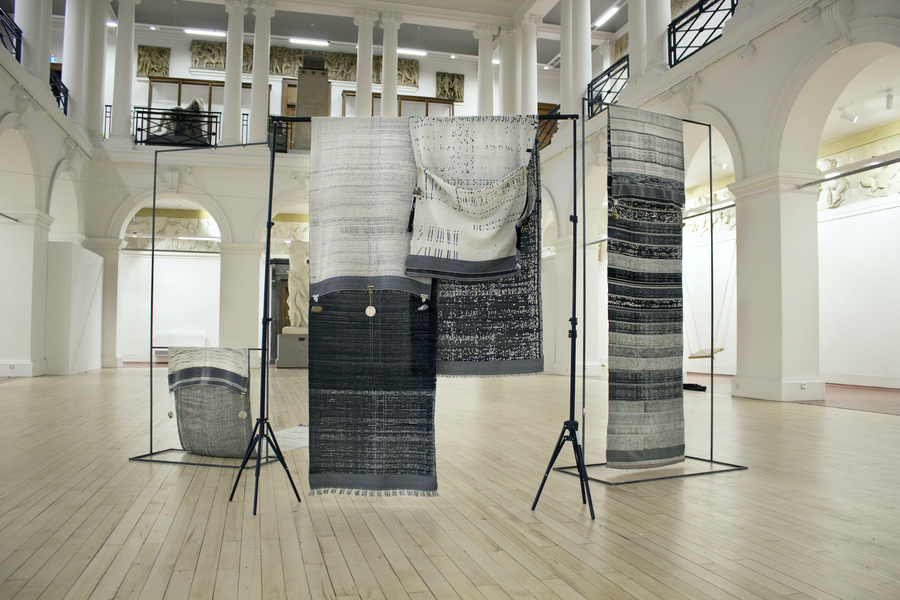 Art piece by Crystal Bennes. Four textile pieces hanging from a series of stands in a white-walled gallery.