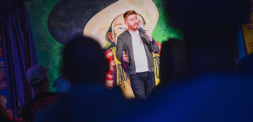 A red-headed man performs stand-up comedy.