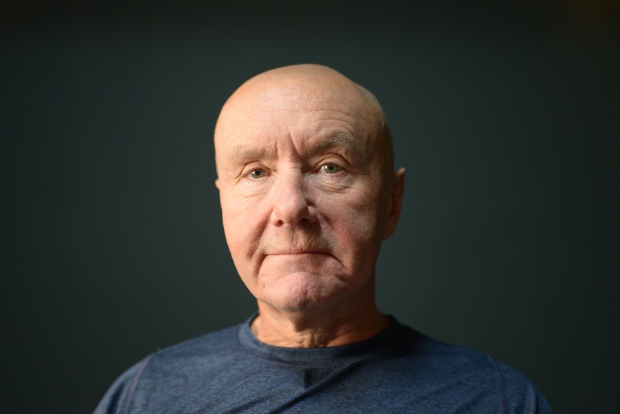 Portrait photo of Irvine Welsh, standing in front of an olive green background.