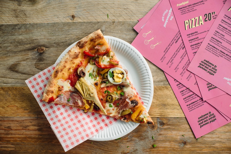 A slice of pizza on a paper plate with a red and white-checked napkin.