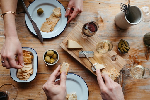 Hands reaching across a table of cheeses and breads.