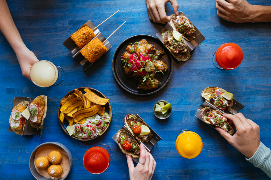 Hands reaching across a blue table to grab from a selection of Mexican dishes.